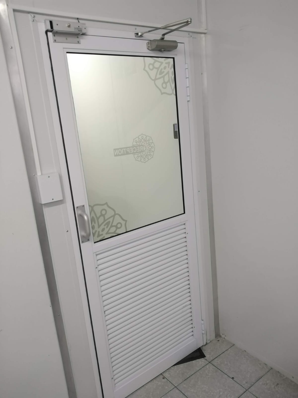 Half-glass, half-aluminium self-closing door leading to staff area at Mubarak Foods, Lansdowne.